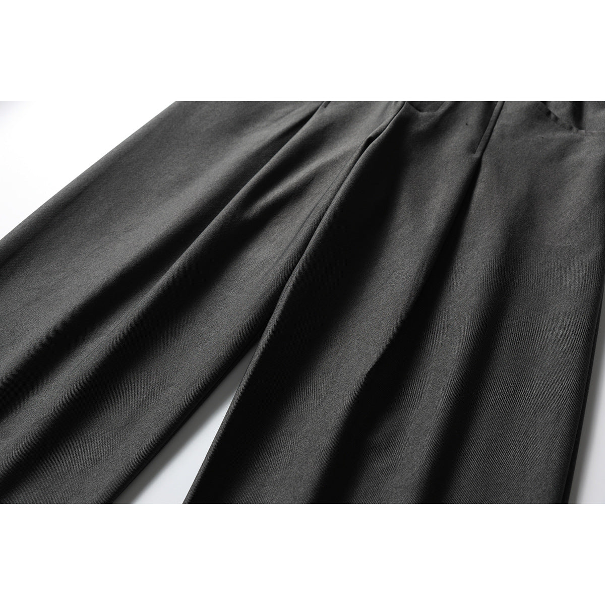Close-up of the dark charcoal trousers' wide legs and front pleats.