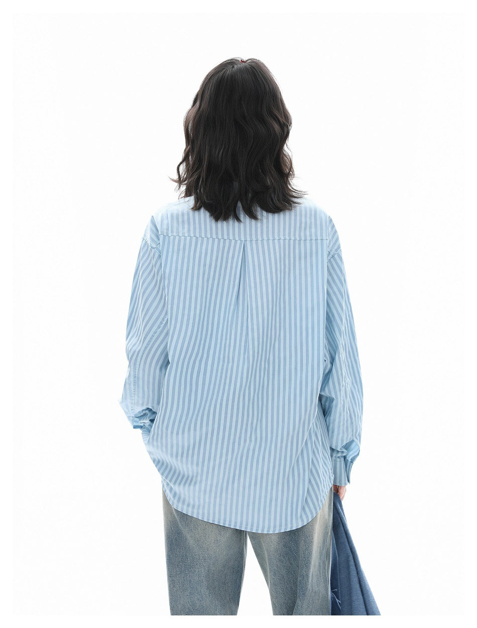 Model shown from behind wearing a loose blue-and-white vertically striped shirt with long sleeves and a curved hem.