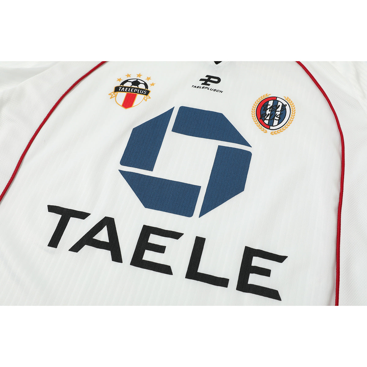 Close-up of a white jersey front showing colorful chest crests, a blue geometric graphic, and black lettering.