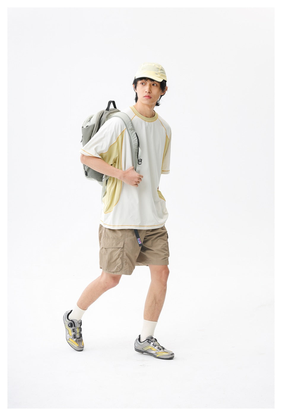 Model wearing a white and pale yellow color-block top and beige cargo shorts, with a backpack.