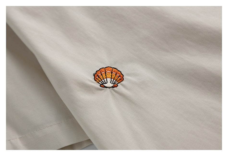 Close-up of an orange-and-white shell embroidery on pale beige fabric.