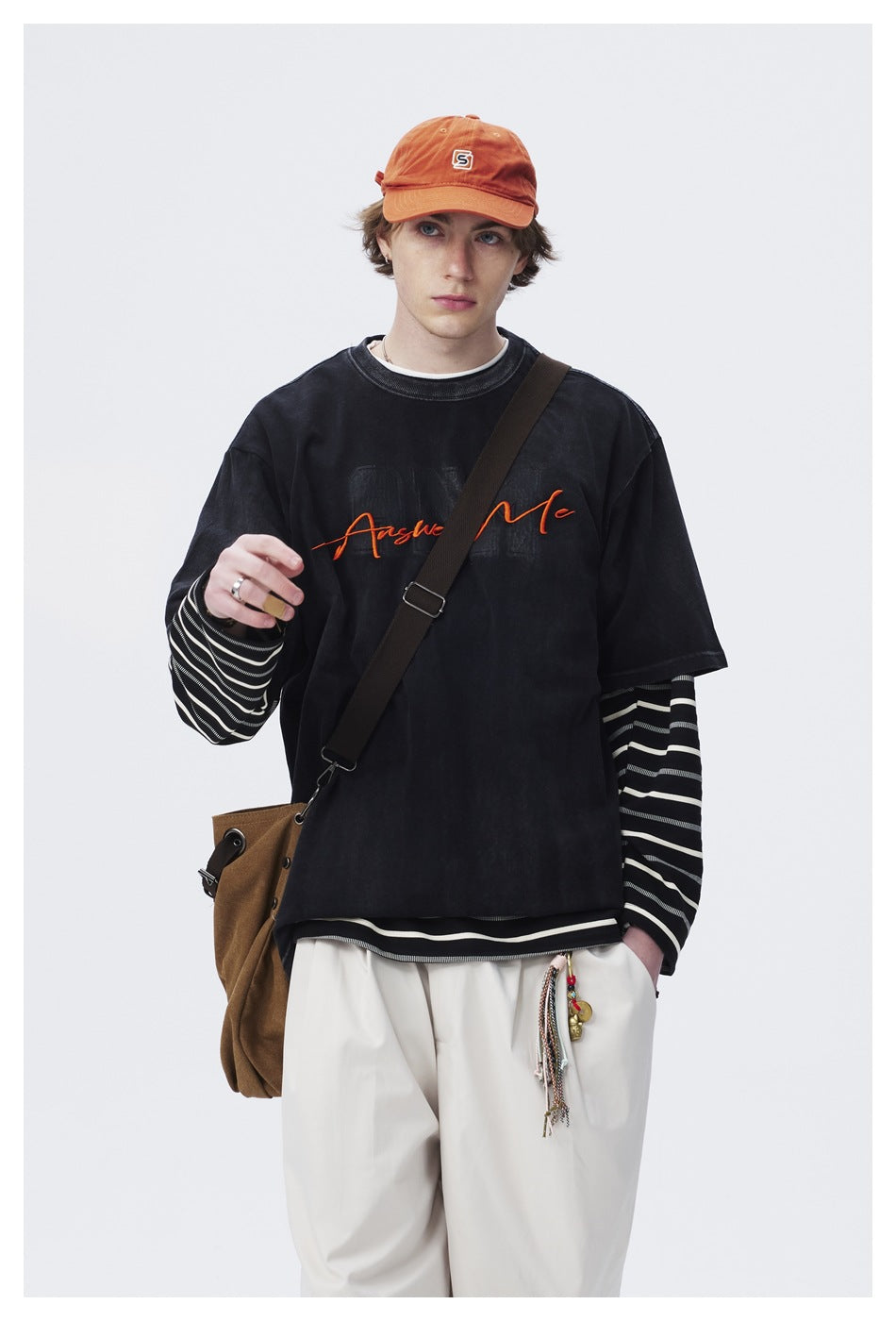 Closer view of a model wearing a black T-shirt with orange script over striped sleeves, paired with loose white pants.