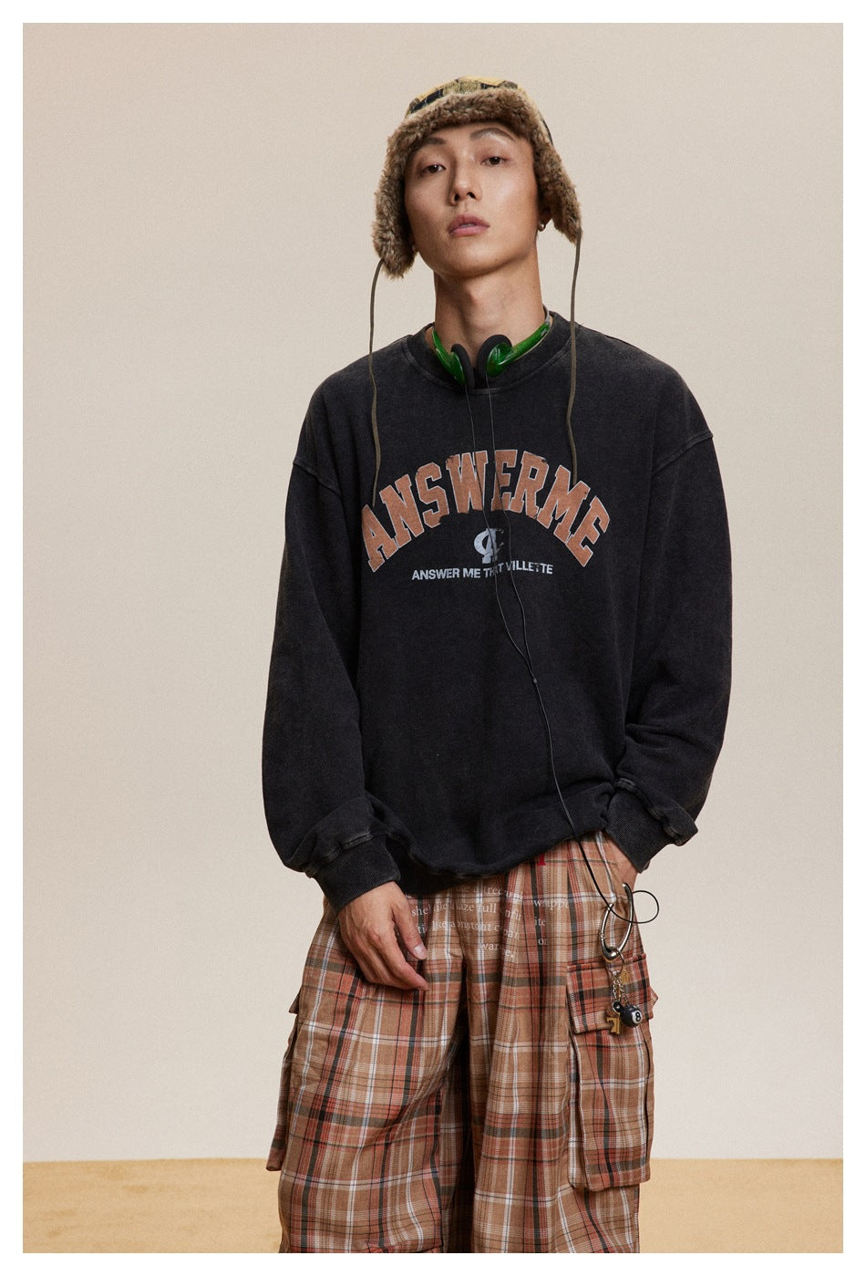 Model wearing a washed black graphic crewneck sweatshirt with brown plaid cargo trousers.