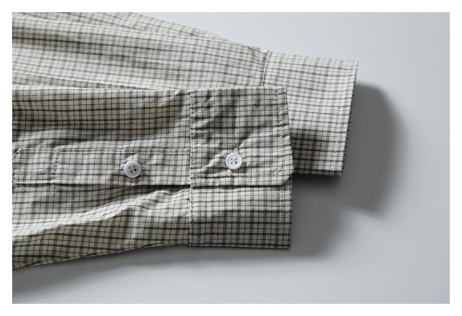 Close-up of a buttoned cuff on the sleeve of an off-white shirt with a fine black and gray check pattern.