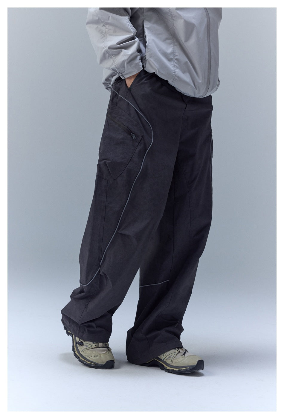 Angled view of loose black cargo pants showing a curved zip pocket and piping.