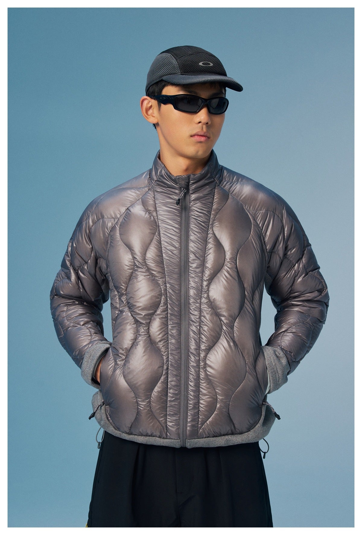 Model wearing a charcoal quilted zip jacket with a high collar, gray cuffs and hem, and curved padded panels.