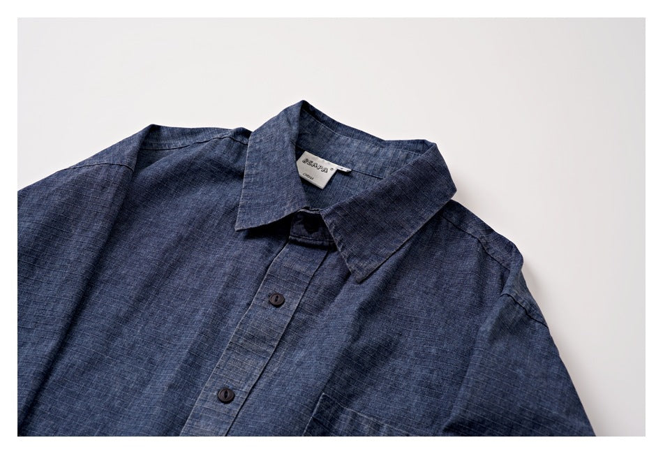 Flat lay of a blue grid-patterned button-up shirt with a pointed collar and dark buttons.