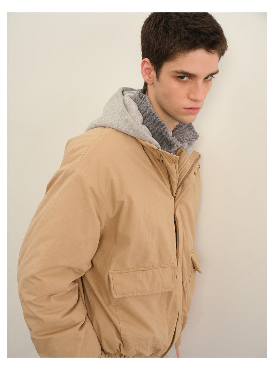 Close angled view of a model wearing a tan hooded jacket, highlighting its sleeve, flap pocket and layered hood.