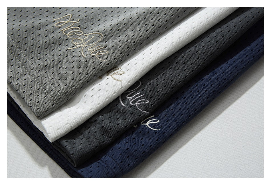 Folded perforated shorts in gray, white, charcoal, and navy, each with embroidered script.