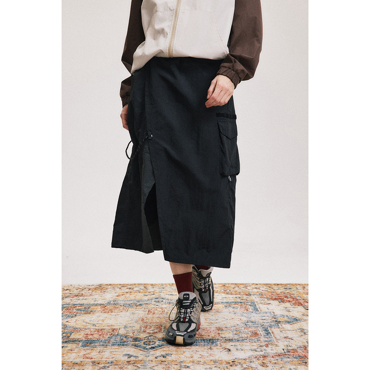 Cropped front view of a model wearing a black mid-calf skirt with a side cargo pocket and front slit.