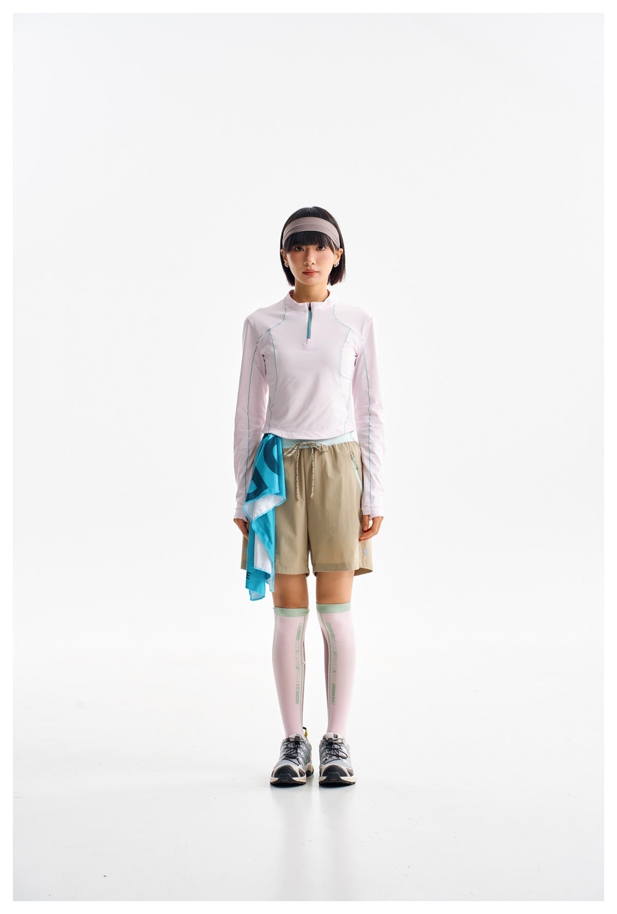 Model wearing a pale pink long-sleeve quarter-zip top with teal seams and tan drawstring shorts.