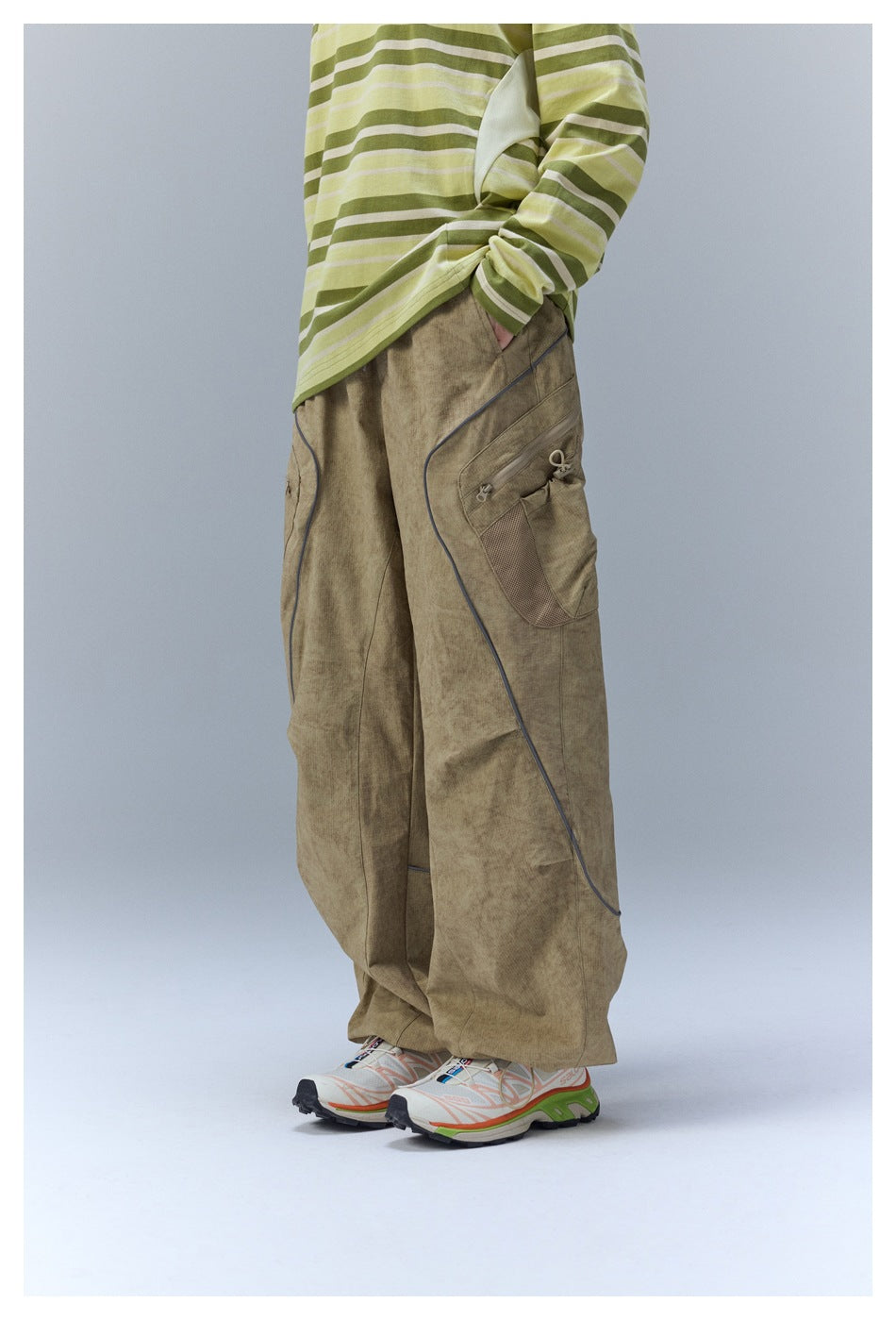 Side view highlighting the loose khaki cargo pants' zippered utility pocket, mesh panel, and curved piping.