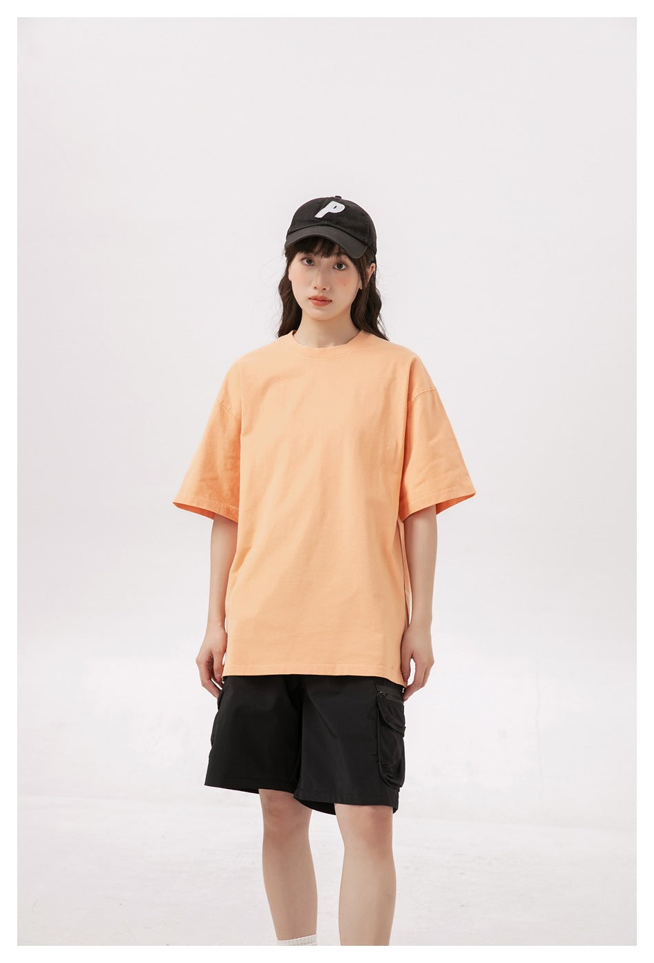 Front view of a model wearing an oversized peach T-shirt and black cargo shorts.