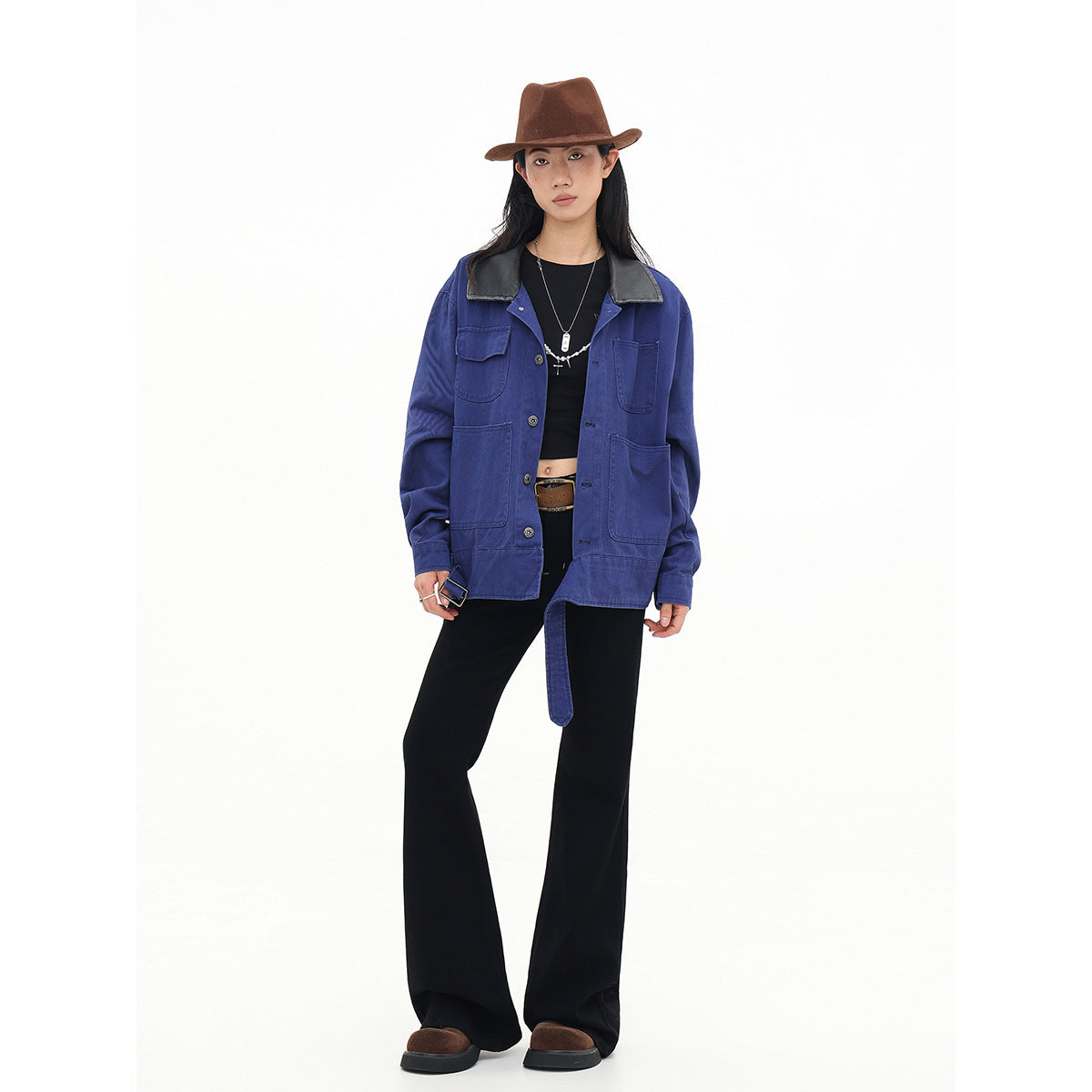 Full-length model wearing an open cobalt-blue utility jacket with a black collar, black flared trousers and a brown hat.