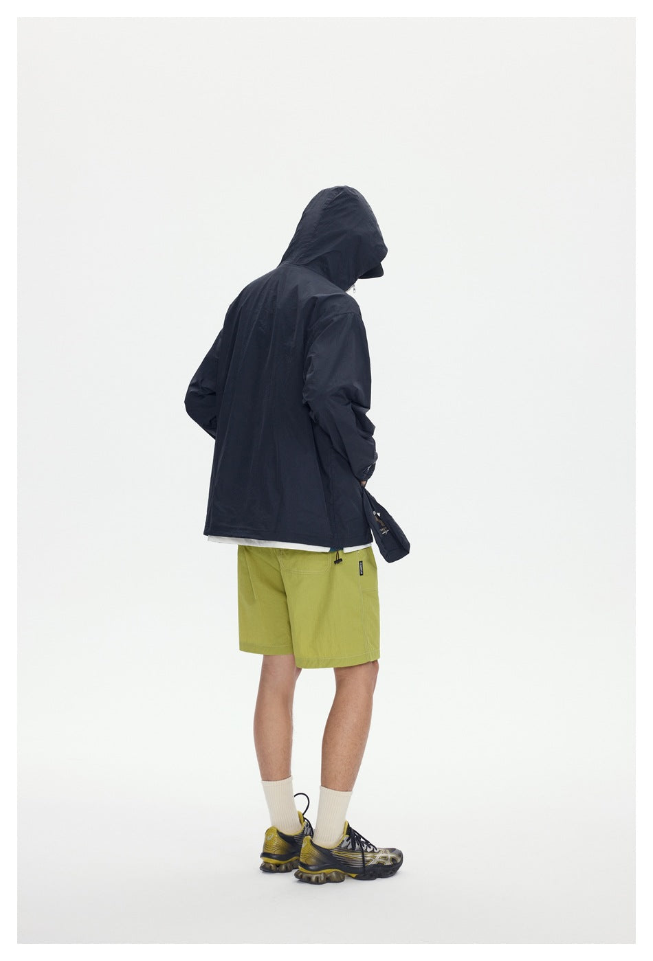 Rear view of a model wearing a dark hooded jacket and lime-green shorts.