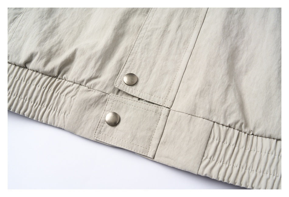 Close-up of a light beige jacket hem with gathered elastic and two metal snap fasteners.