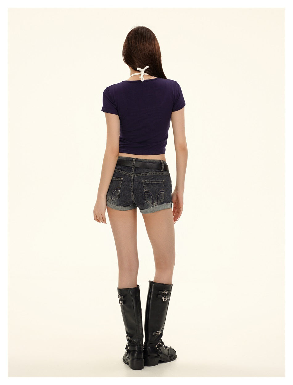 Back view of a model wearing a plain navy cropped tee over a white halter top, with dark denim shorts.