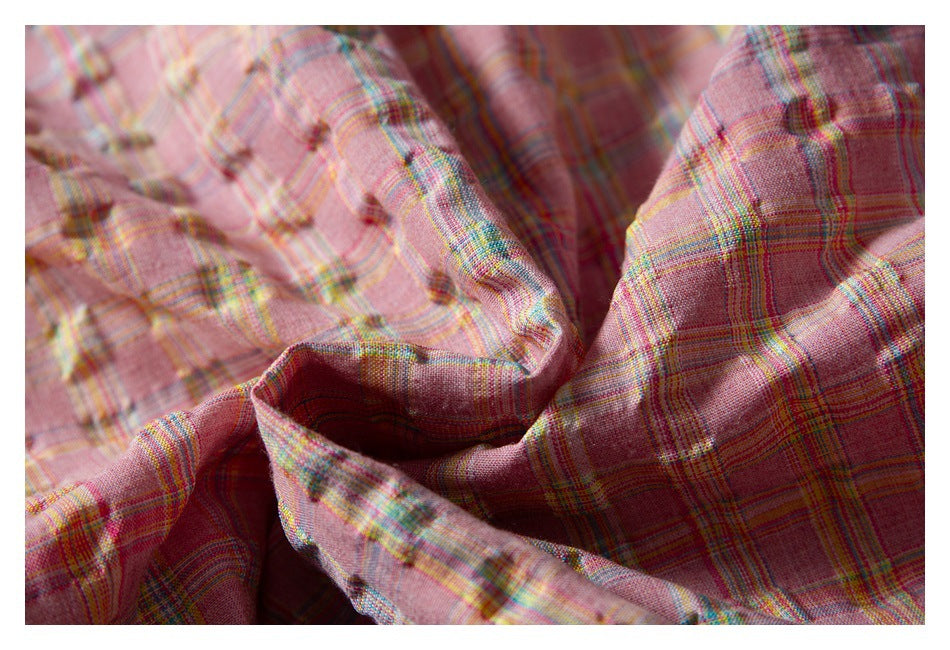 Close-up of pink plaid garment fabric folded to show its pattern, texture, and stitching.