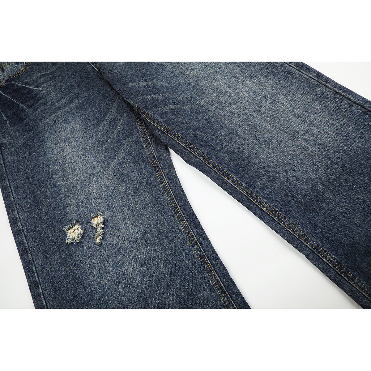 Close-up of dark blue jeans legs with two frayed tears and contrasting golden stitching.