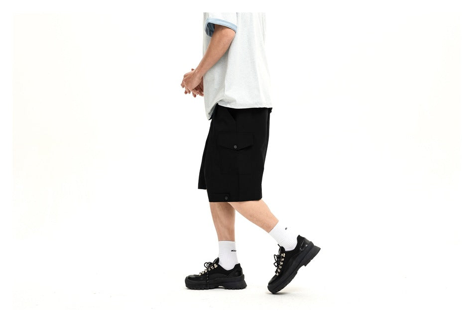 Side view of a model wearing black cargo shorts with a flap cargo pocket.
