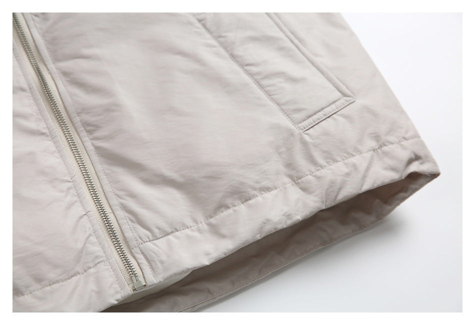 Close-up of the light beige jacket's front zipper, pocket, and stitched hem.