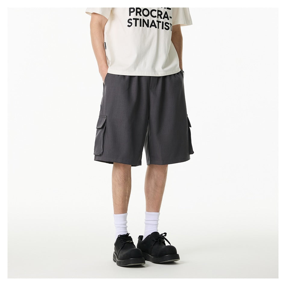 Front view of a model wearing loose charcoal-gray cargo shorts with large flap pockets on both sides.