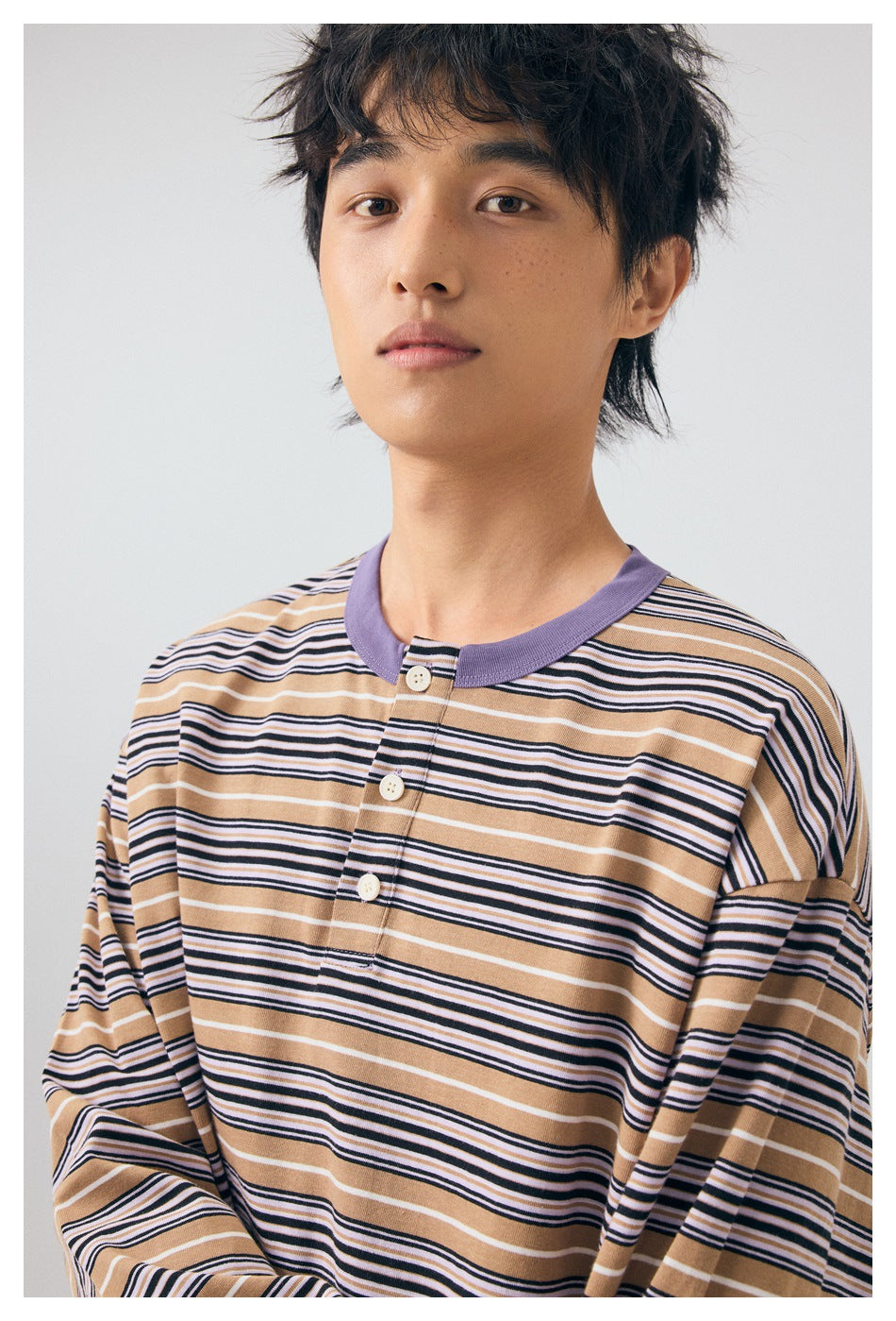 Close view of a model wearing a tan, navy, and white striped henley with a purple collar and three-button placket.