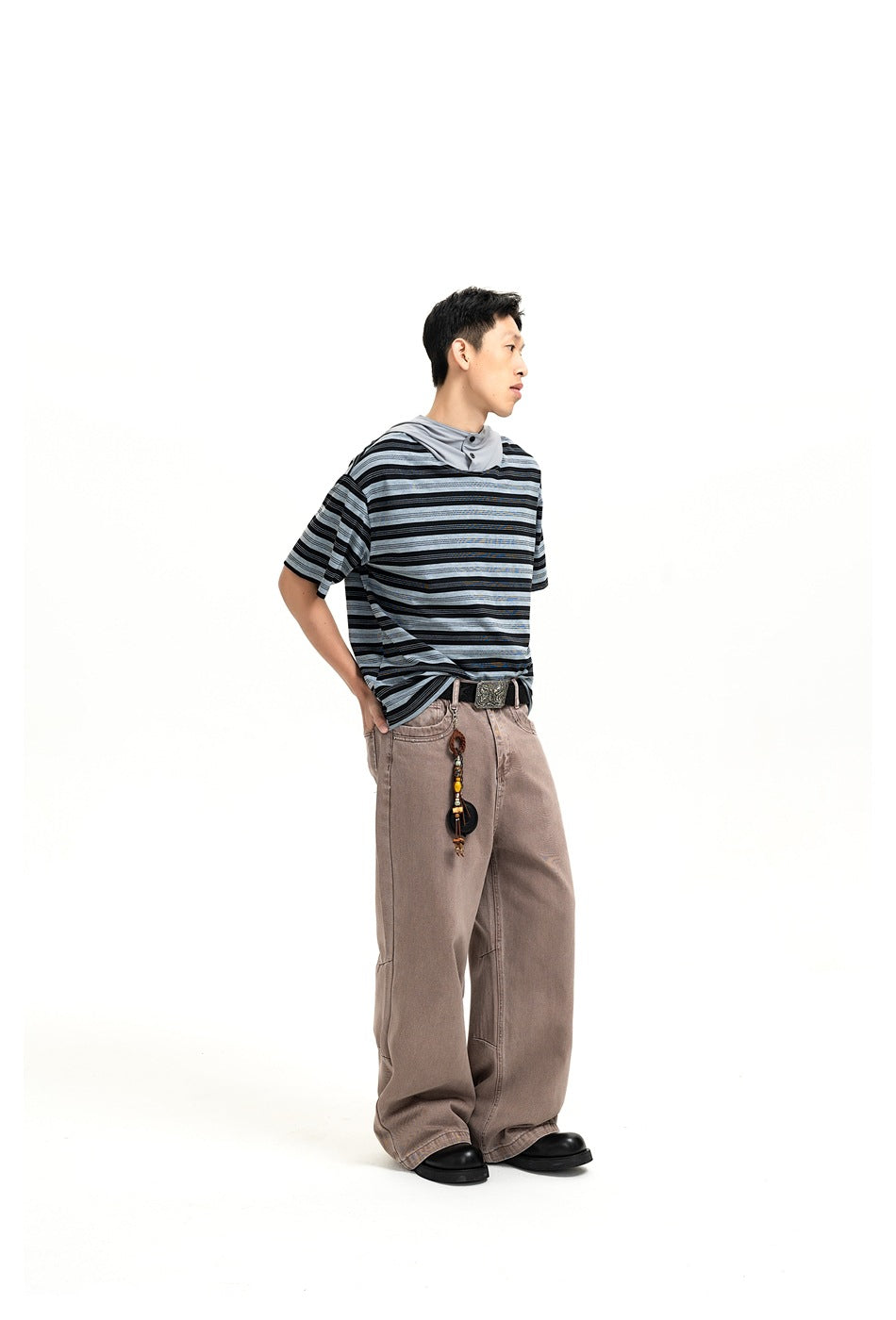 Man in profile wearing a striped short-sleeve hooded top with brown wide-leg pants and black boots