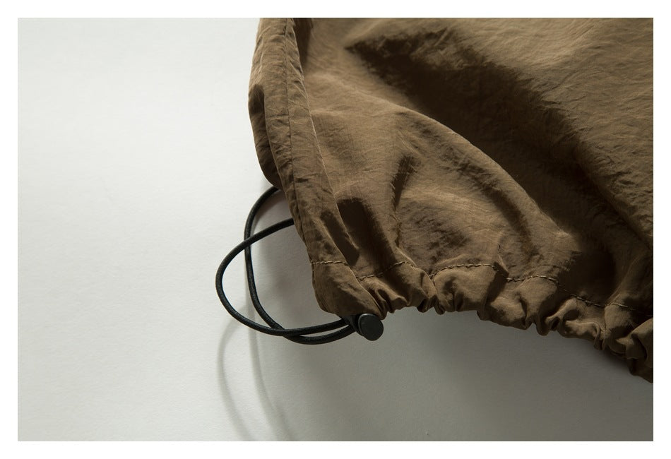 Close-up of a gathered brown garment hem with a black elastic drawcord and toggle.