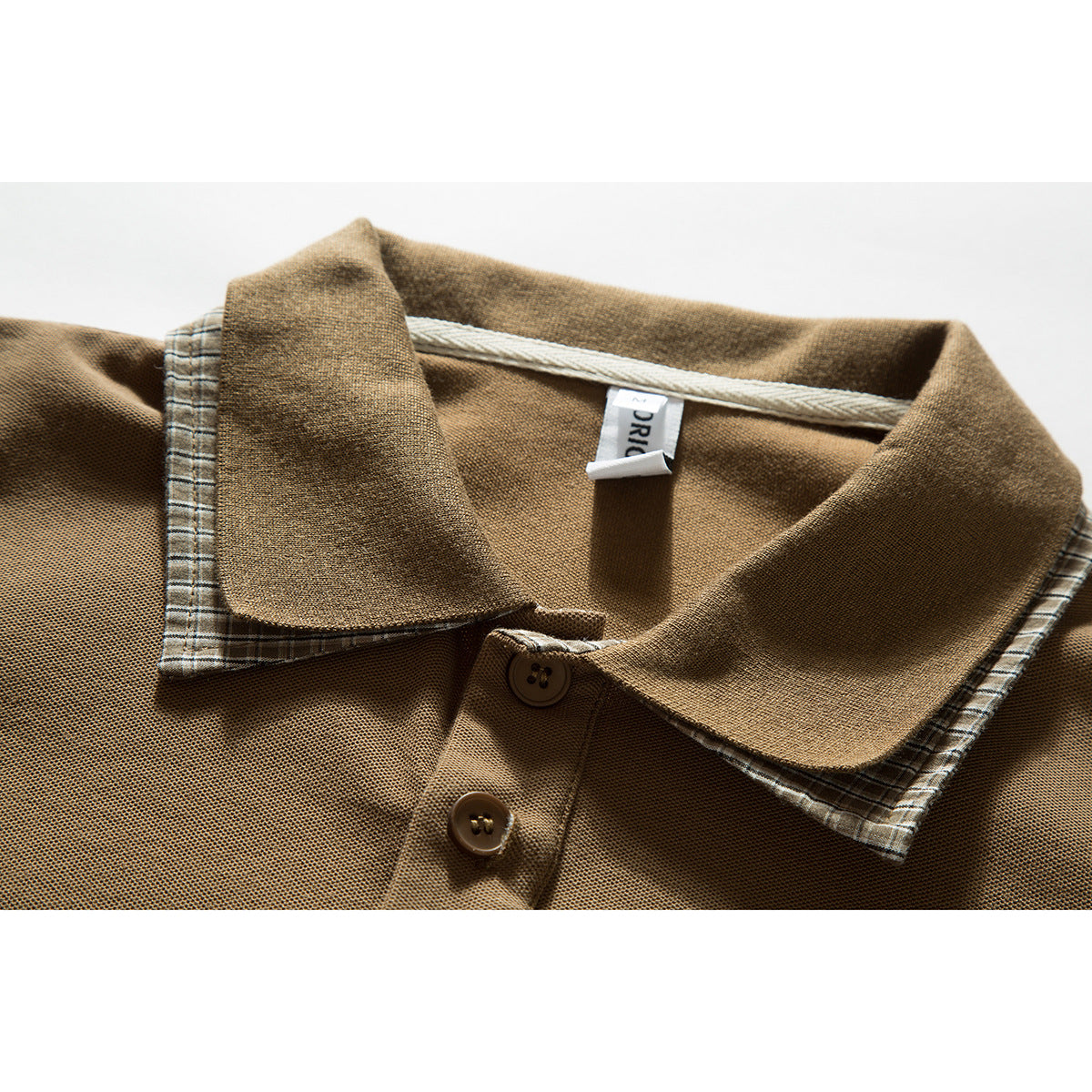 Close-up of a tan polo shirt collar with plaid underside, a two-button placket, and a small neck label.