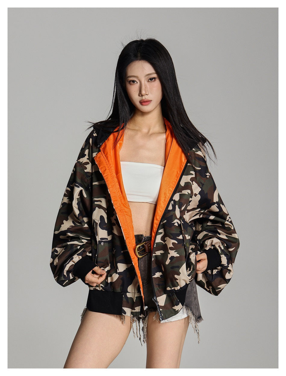 Model in open camouflage jacket showing bright orange lining, black ribbed cuffs and hem, with white top and denim shorts