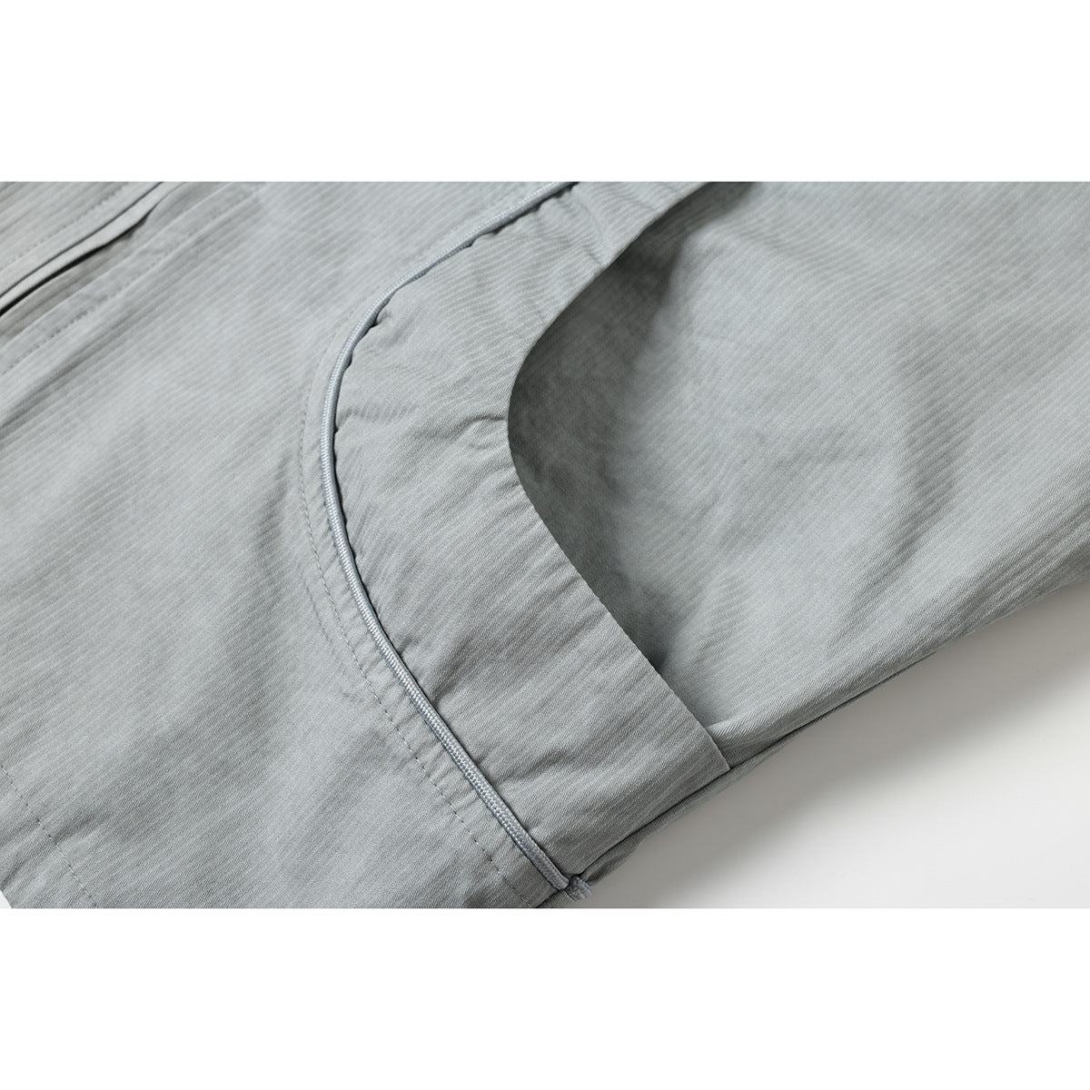 Close-up of a light gray jacket's curved side pocket opening and bound seam.
