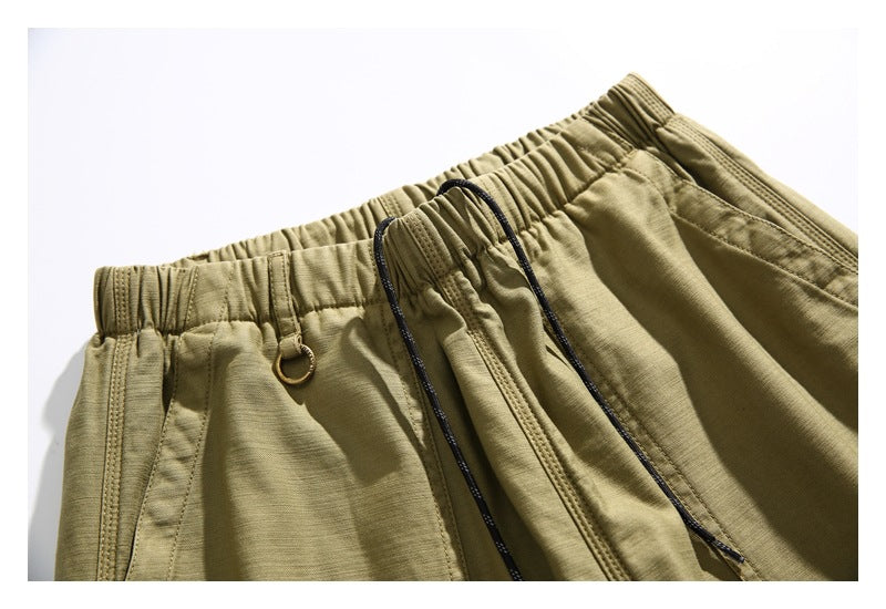 Close-up of olive shorts showing the elastic waistband, dark drawstring, and small metal ring.