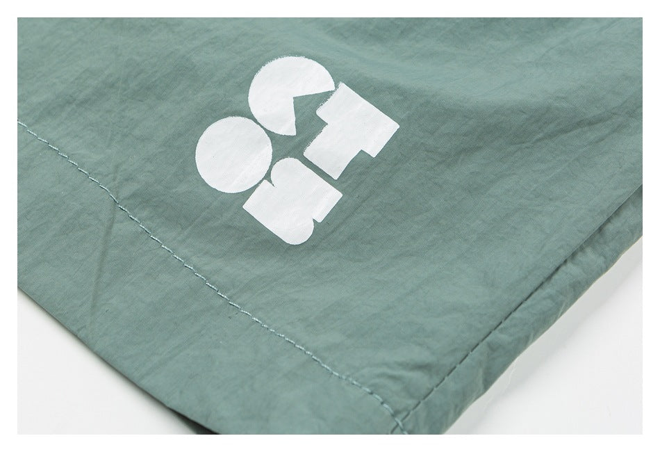 Close-up of sage green shorts with a small white abstract graphic near the stitched hem.