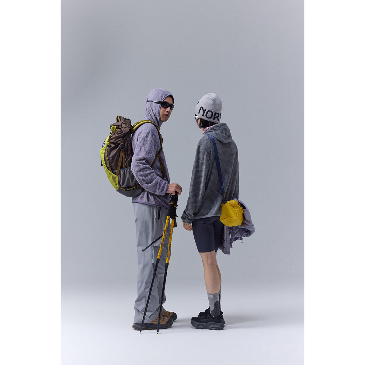 Two hikers model a lavender hooded pullover and gray fleece top with chest pocket, paired with hiking pants and shorts.