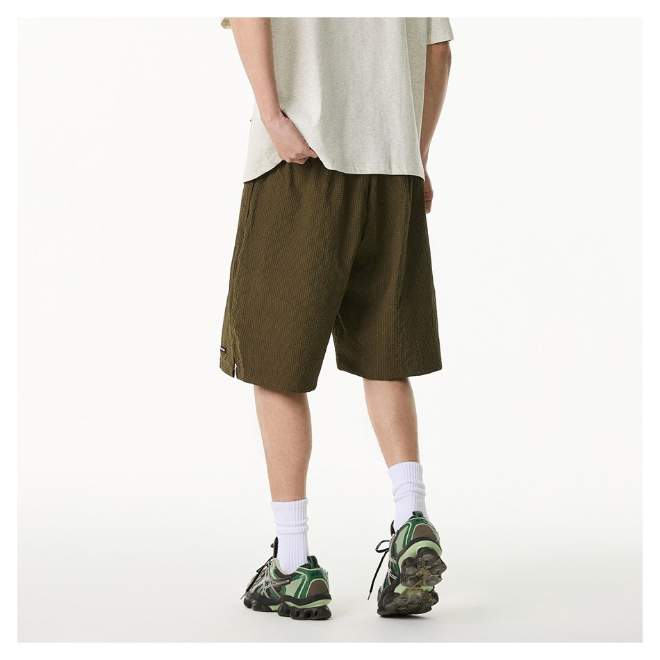 Rear view of a model wearing olive textured knee-length shorts with a light T-shirt and sneakers.
