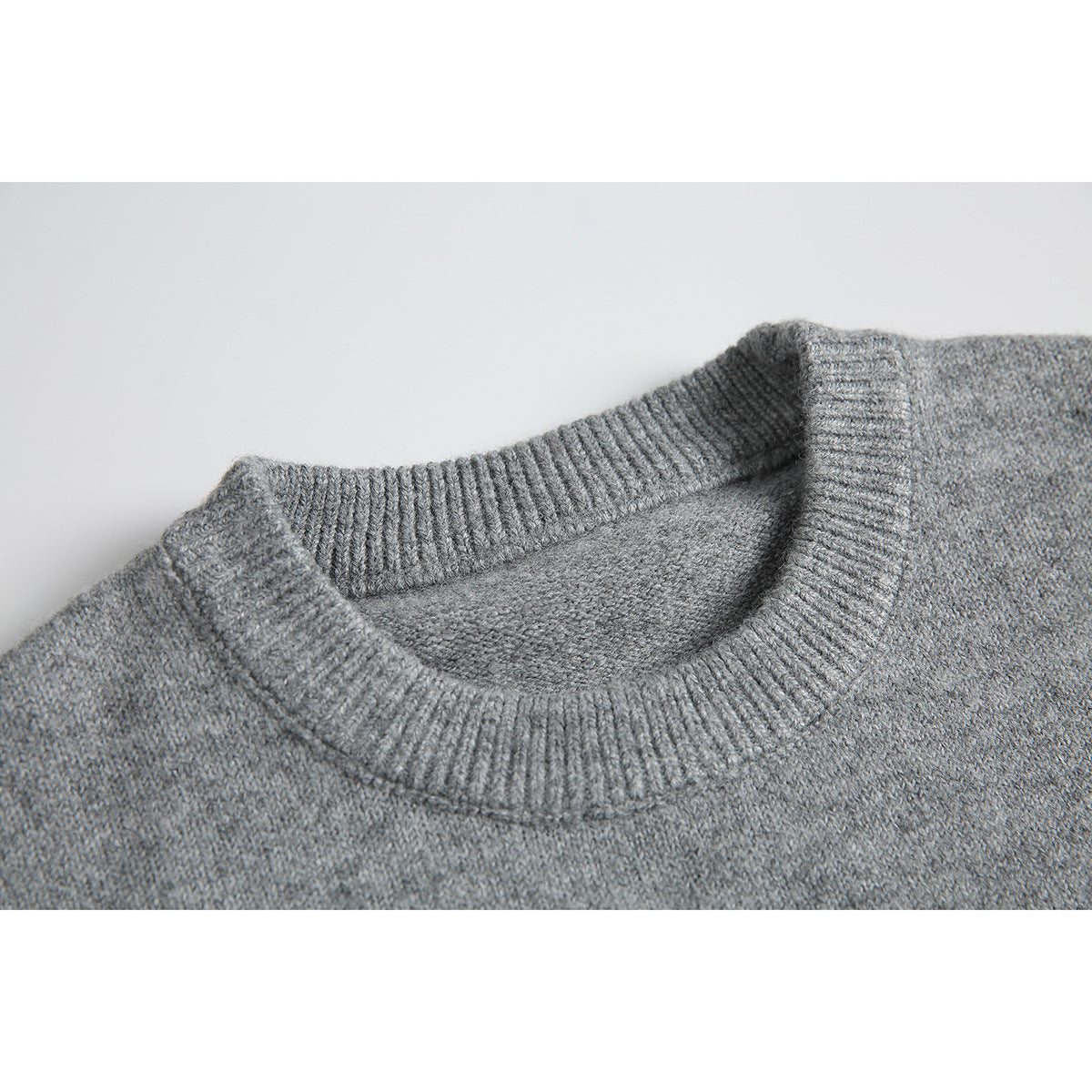 Close-up of a gray knit sweater's ribbed crew neckline and textured body.