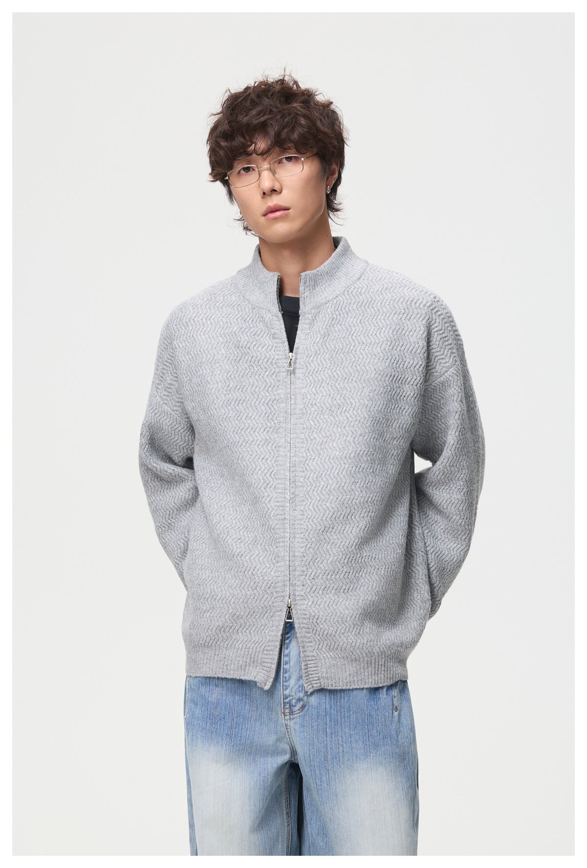 Model wearing a light gray textured zip-front cardigan with a stand collar and blue jeans, shown from the front.