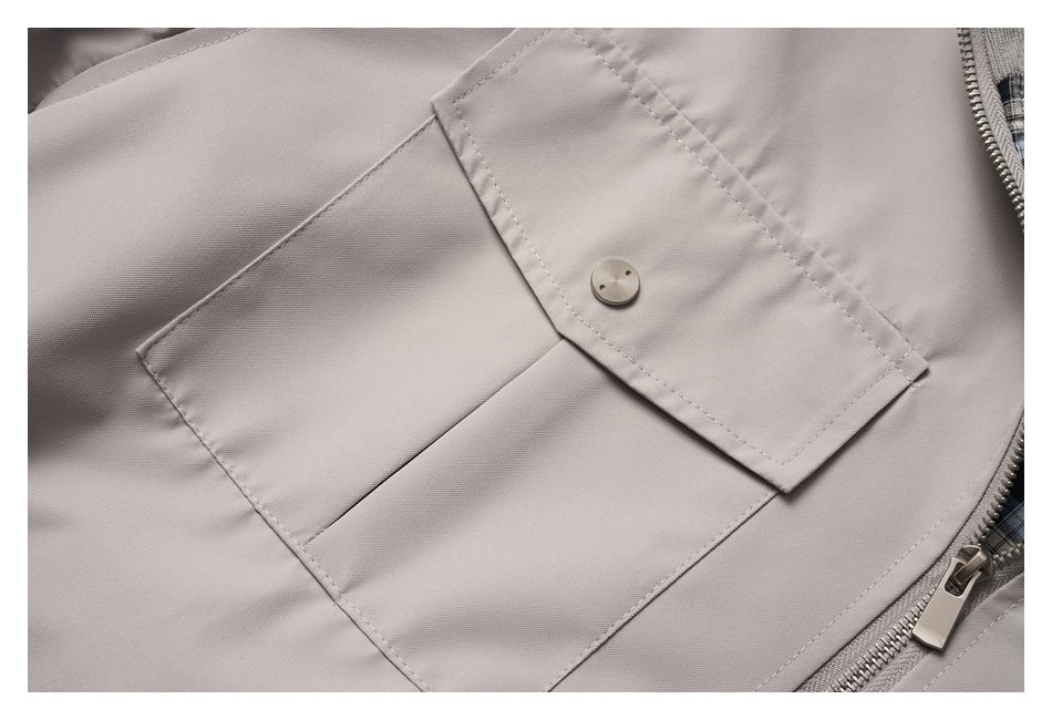 Close-up of a light taupe jacket's flap pocket, button, stitching, and front zipper.