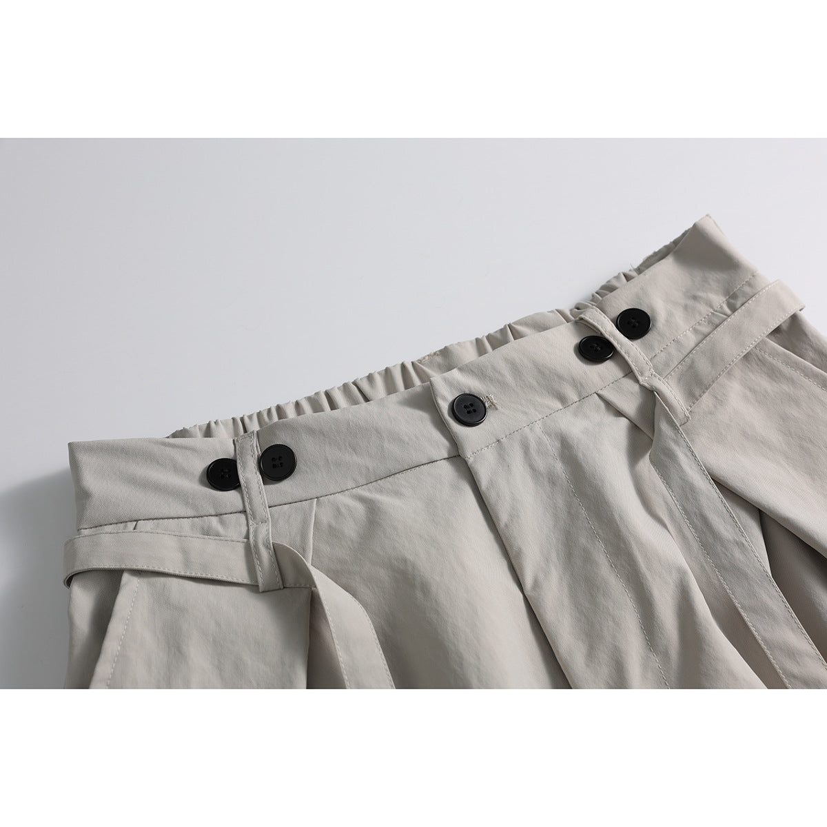 Close-up of light beige wide-leg trousers showing the gathered waistband, black buttons, belt loops and matching belt.
