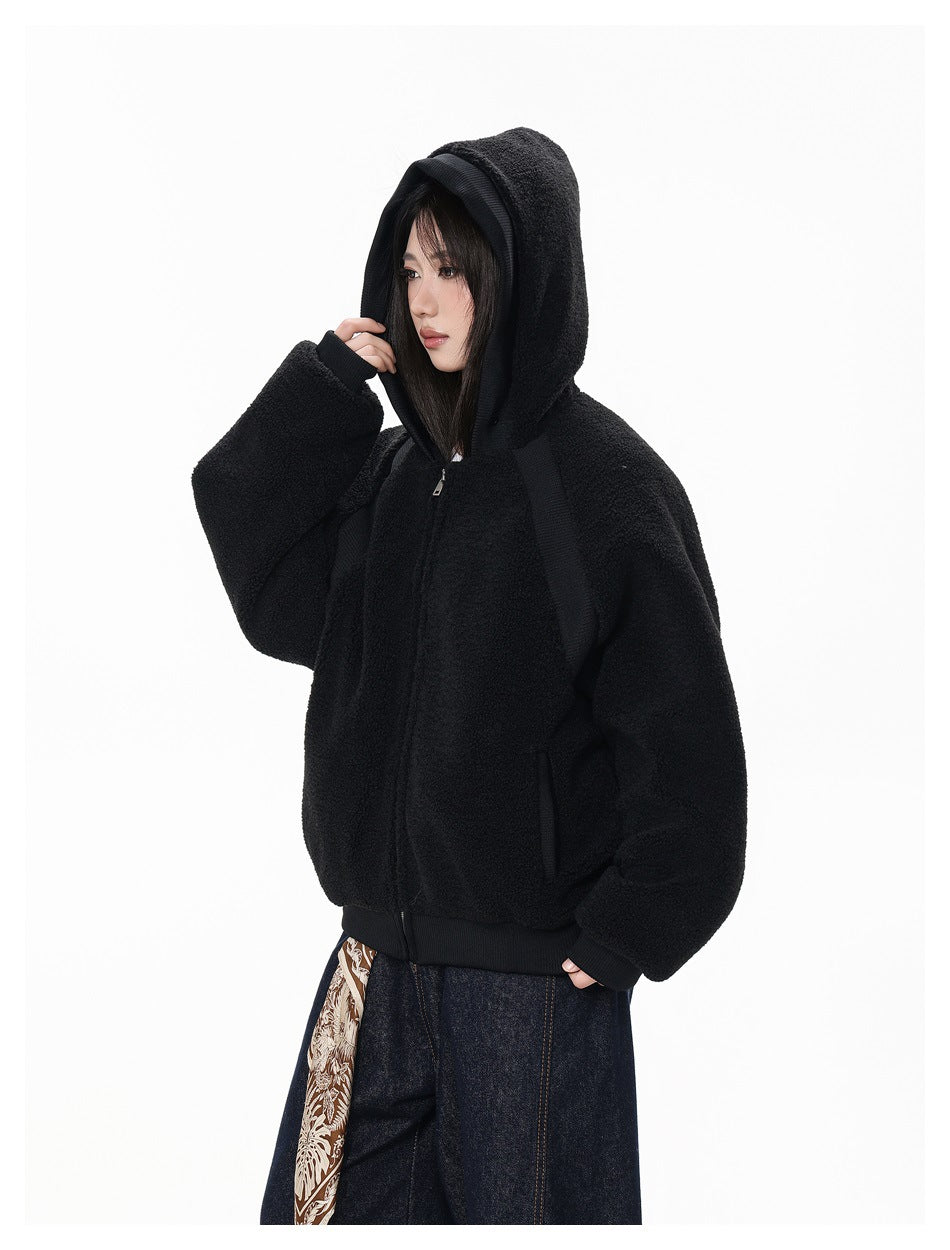 Three-quarter side view of a model wearing a black plush zip-up hoodie with the hood raised.