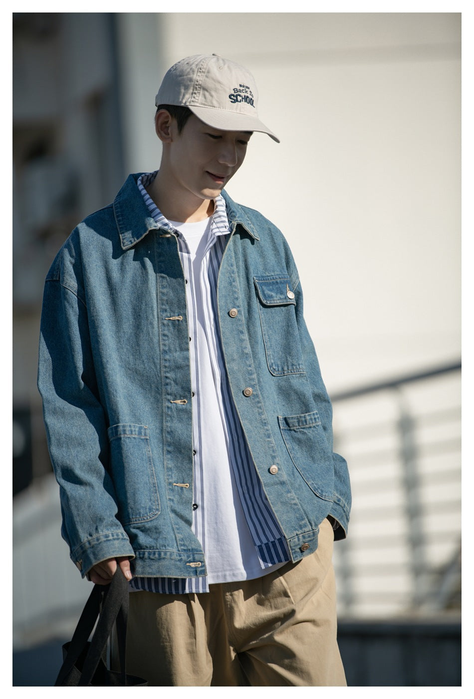 Model wearing a blue denim jacket over a striped shirt and white tee, shown from the waist up.