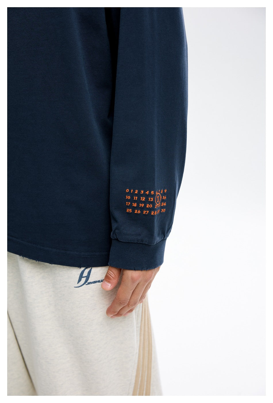 Close-up of the navy sleeve showing a small orange calendar-style graphic and ribbed cuff.