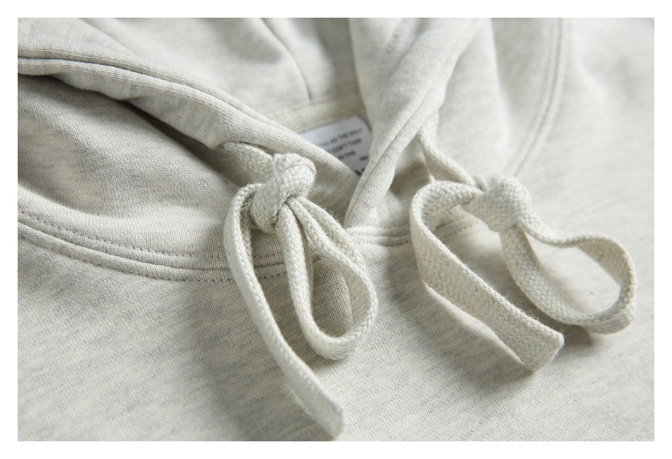Extreme close-up of the thick cream drawstrings and hood stitching on a light gray hoodie.