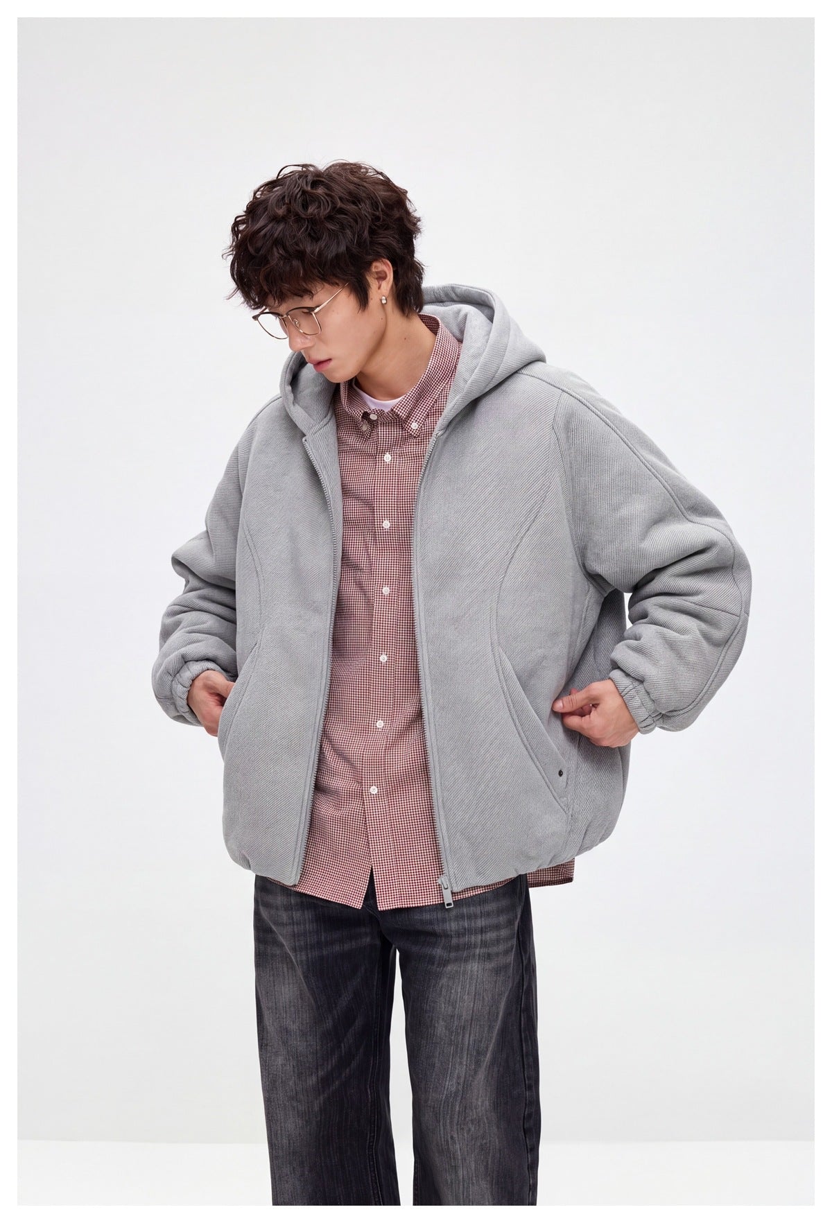 Model in light gray hooded zip jacket over a red checked shirt, looking down with hands at the pockets