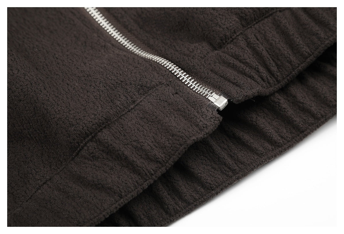 Close-up of the zipper ending above a stitched seam on dark brown textured fabric.
