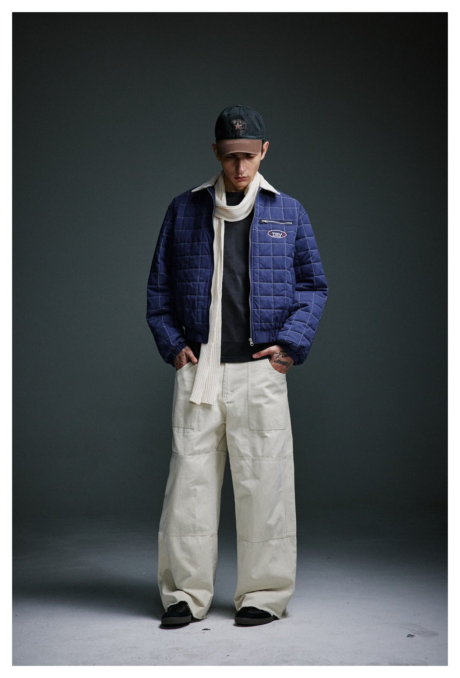 Model wearing a navy quilted jacket with cream collar, long cream scarf and wide cream trousers.