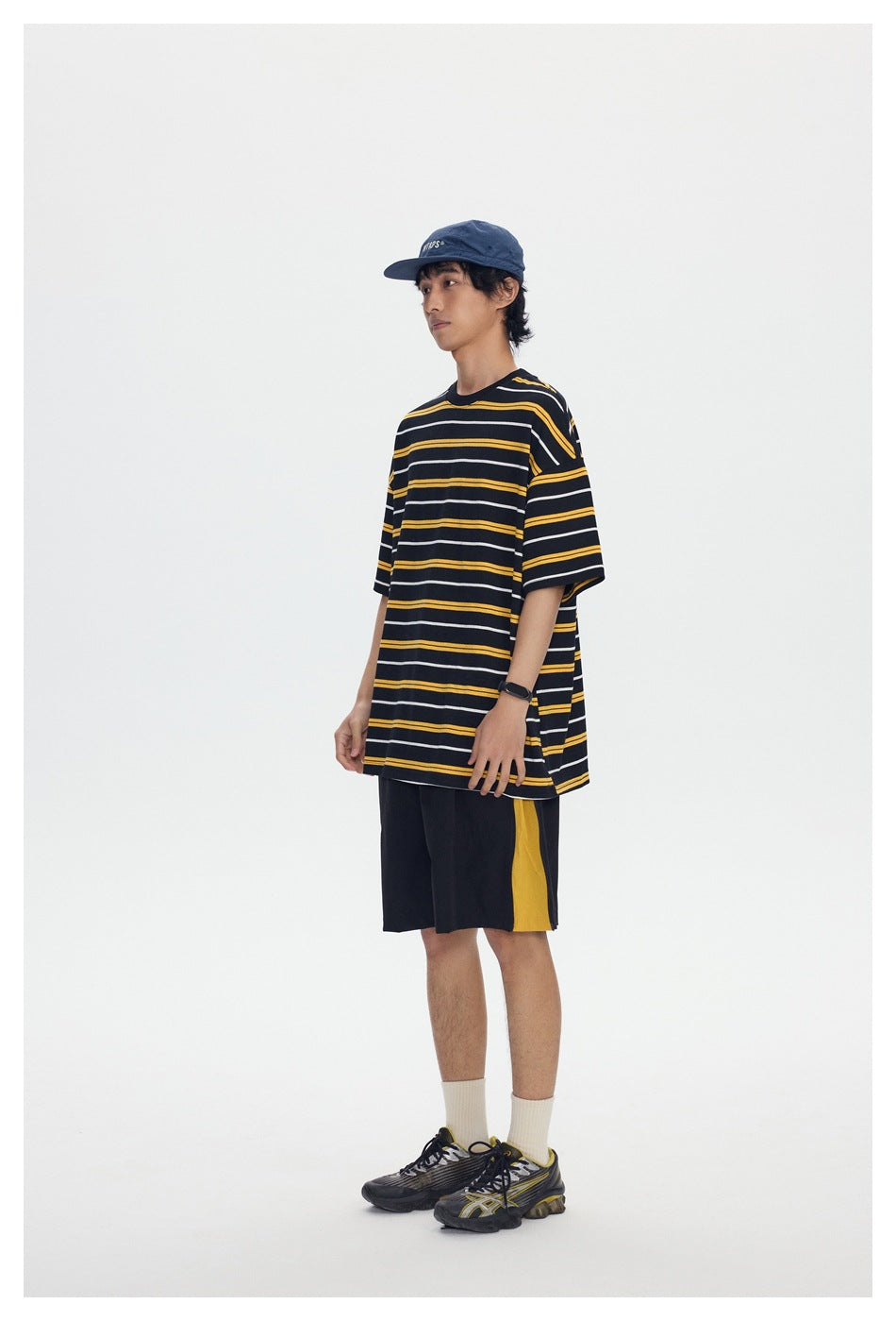 Model wearing a black T-shirt with yellow and white horizontal stripes and black shorts with a yellow side panel.