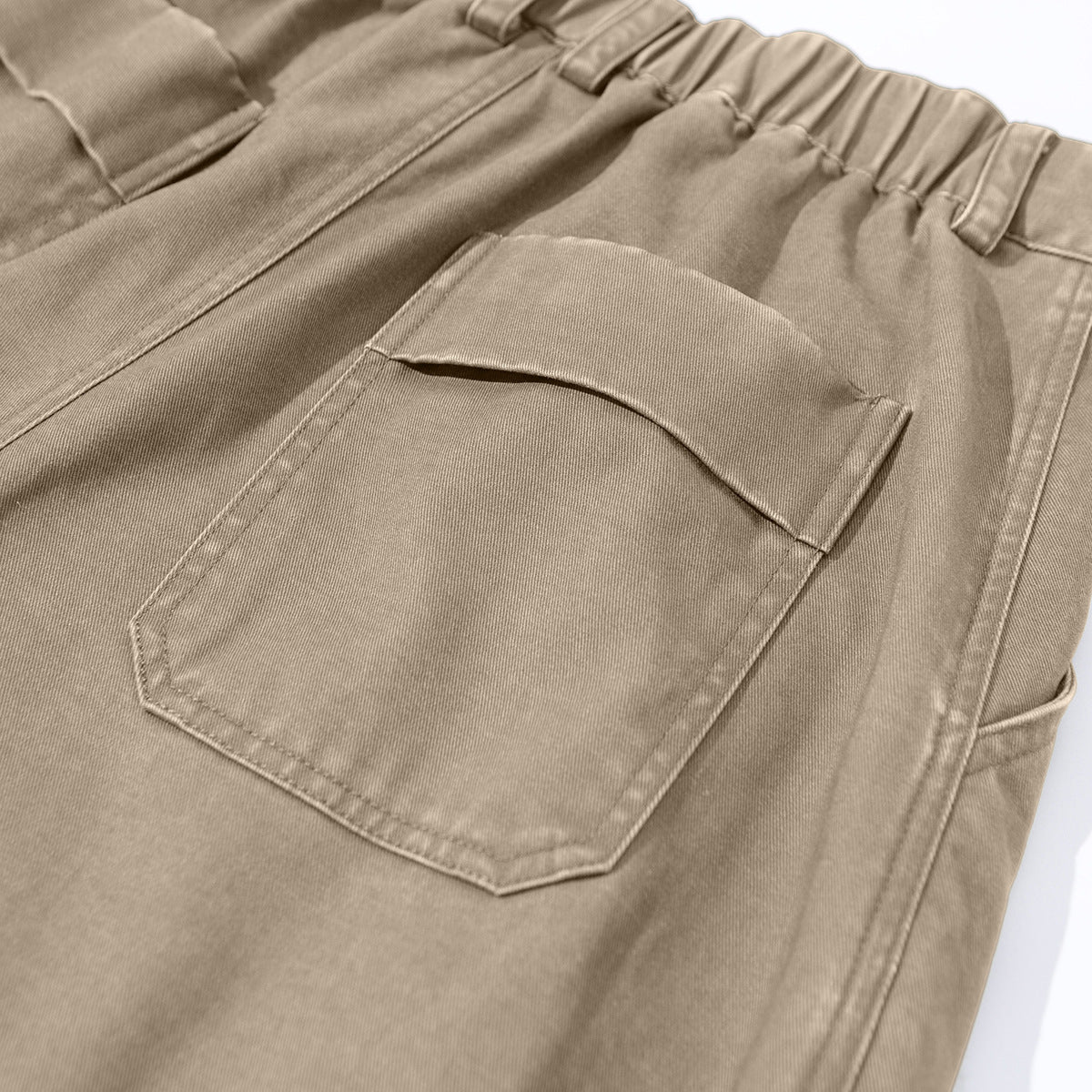 Close-up of taupe trousers showing a flap back pocket and gathered elastic waistband.