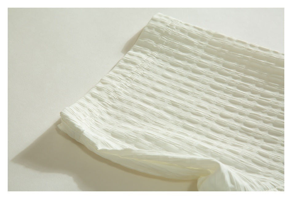 Close-up of a gathered, folded edge on the textured ivory garment.